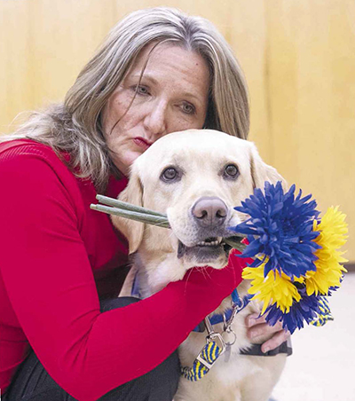 Person hugging Canine Companions service dog who is holding flowers in it's mouth