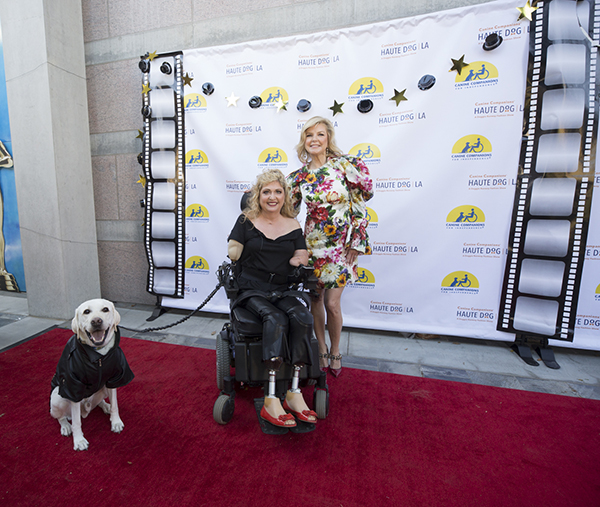two people and a Canine Companions service dog on a red carpet