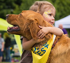 Young girl hugging golden retriever wearing a Canine Companions DogFest bandanna
