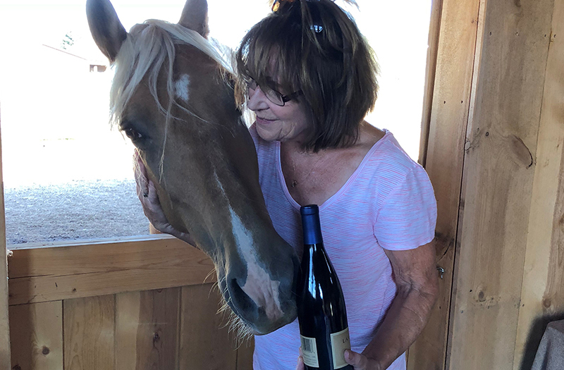 Woman holding a wine bottle hugging a horse