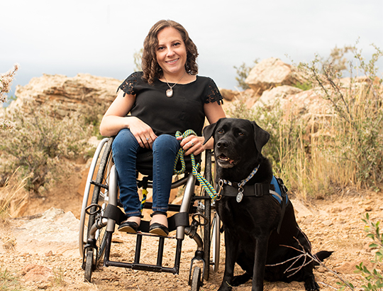 woman sitting in wheelchair with a Canine Companions service dog sitting next to her