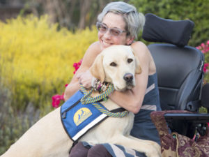 Woman sitting in wheelchair hugging a yellow Canine Companions Service Dog