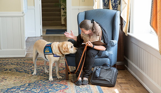 Woman sitting in chair with her Canine Companions Hearing Dog by her side