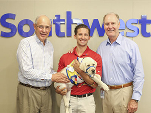 three people standing in front of Southwest logo holding a Canine Companions puppy