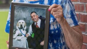 Woman holding framed photo of man and his service dog