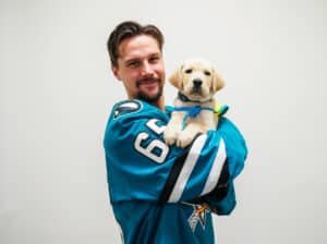 Jan Jose Sharks player in a jersey holding a yellow lab puppy in a yellow service vest