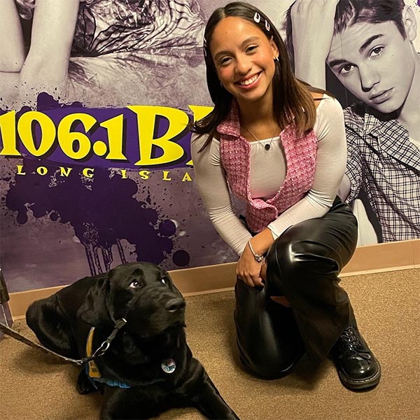 black lab puppy in yellow vest at the WBLI music studio next to a smiling girl