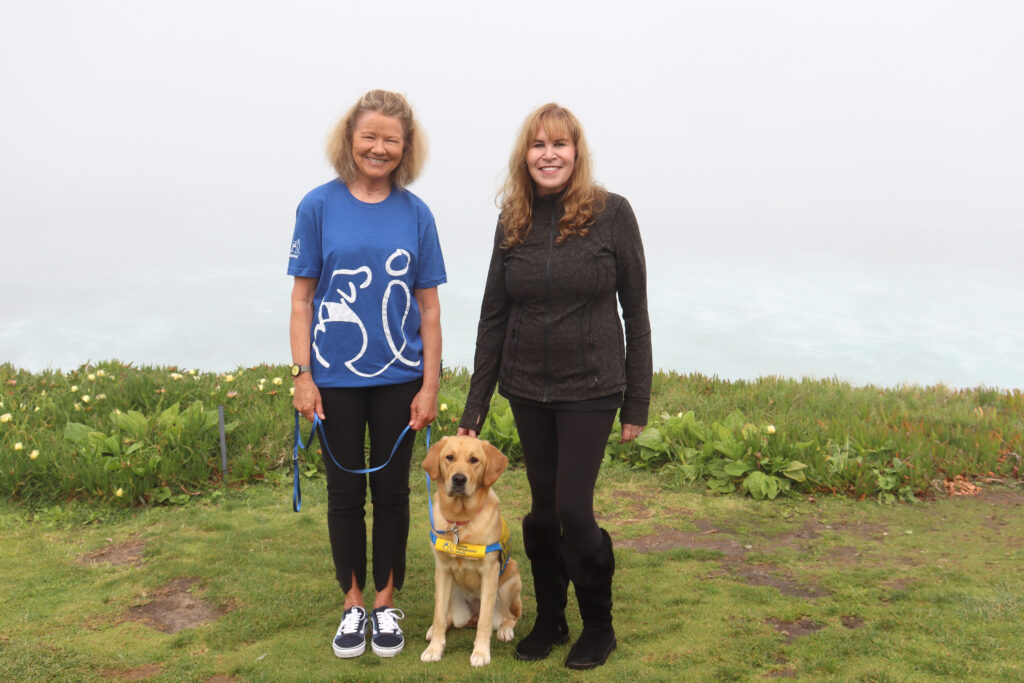 Two woman standing and smiling with yellow lab sitting between them
