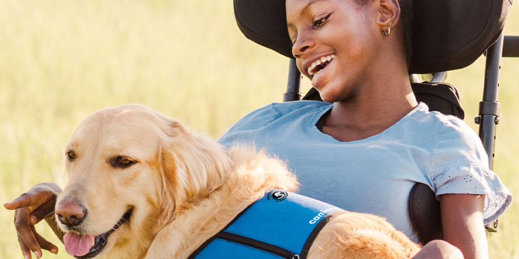 Girl in a wheelchair with a Golden Retriever in a blue service vest laying across her lap