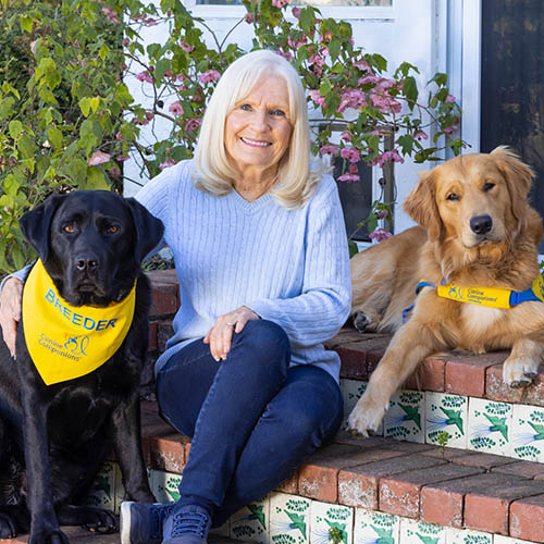 Portrait of Kathy Zastrow sitting between two dogs with yellow Canine Companions vests