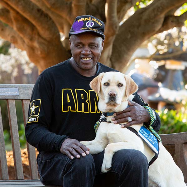 African american man in a sweatshirt with US Army logos with a yellow lab service dog in blue vest laying in his lap