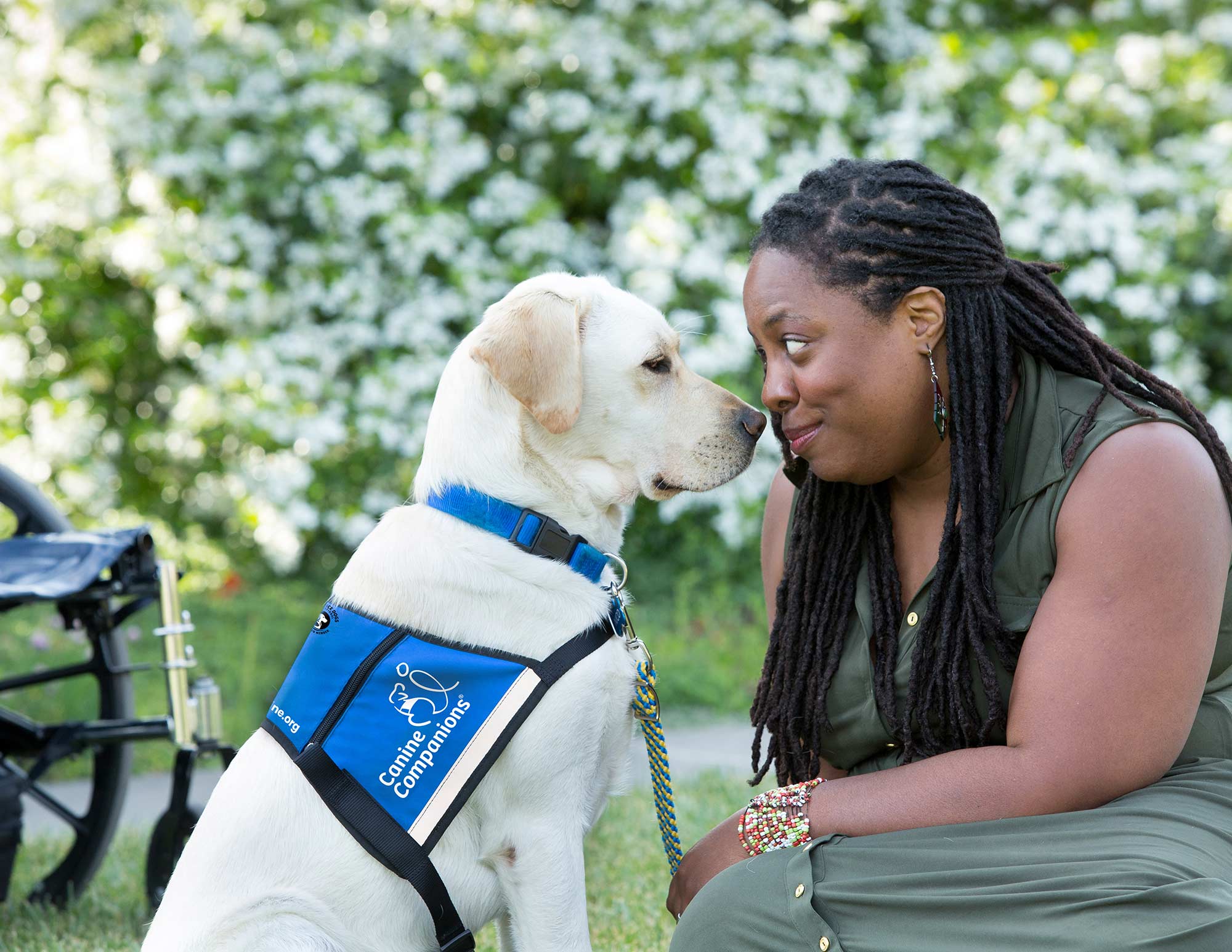woman sits nose to nose with yellow lab service dog in blue vest