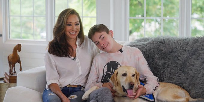 A woman with her son sit on a sofa with their yellow lab service dog