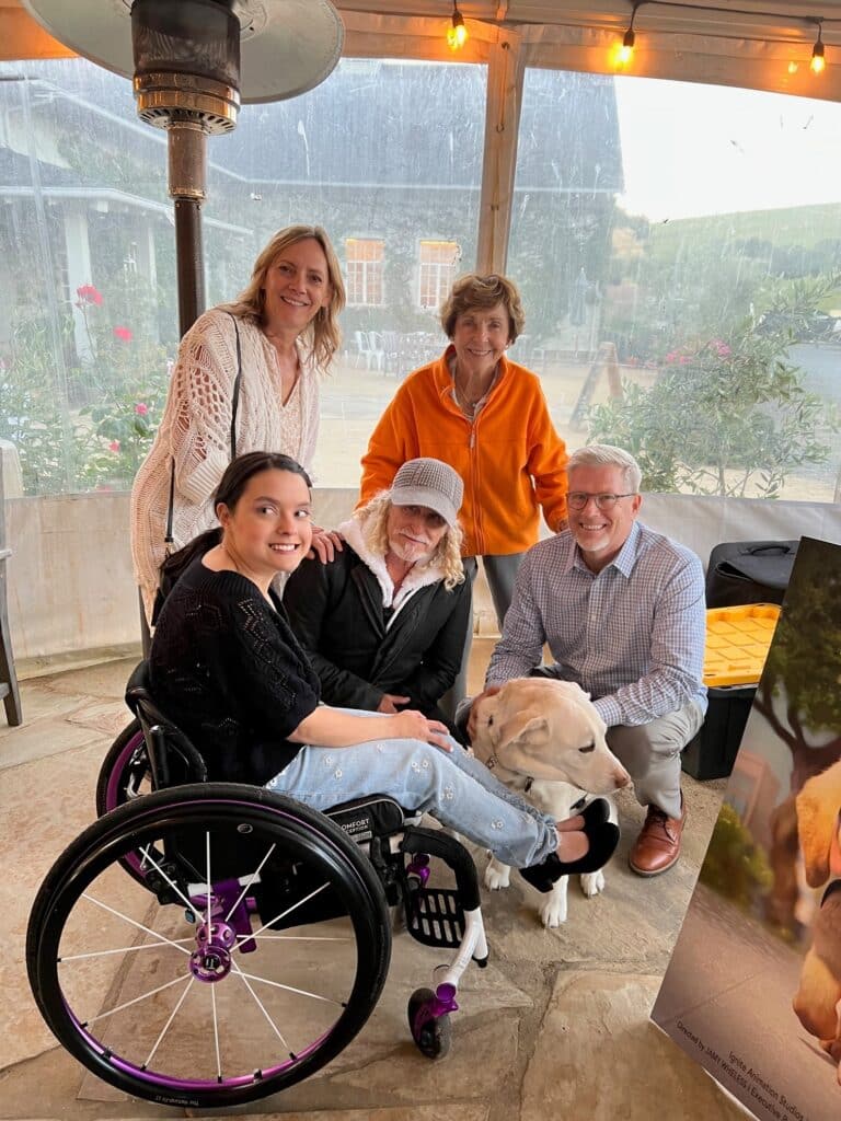 a group of people around a young woman in a wheelchair and her yellow lab service dog