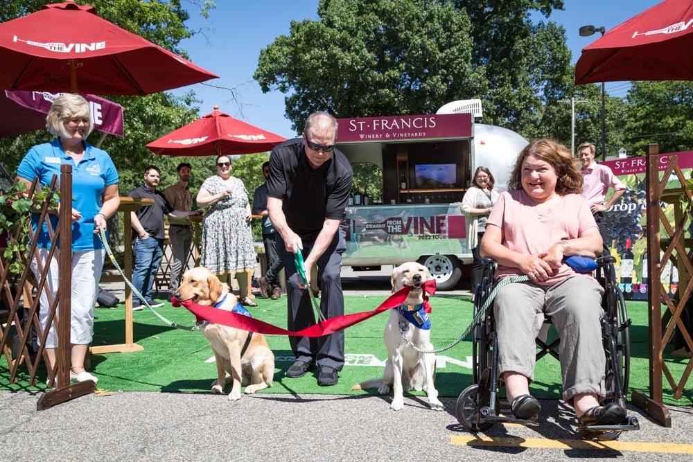 two service dogs holding a ribbon that is being cut