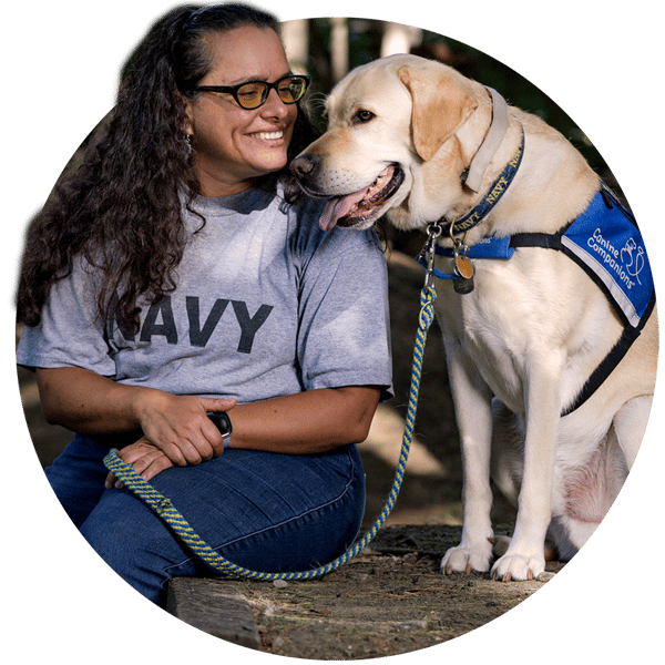 Woman sits next to a yellow lab service dog wearing a blue vest
