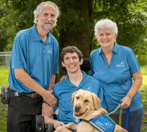 Young man in wheelchair and service dog on his lap with his parents next to him