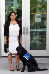 Woman standing next to a facility dog in front of the district attorney's office