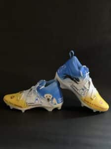 Blue and yellow cleats showcase Canine Companions logo and service dogs.