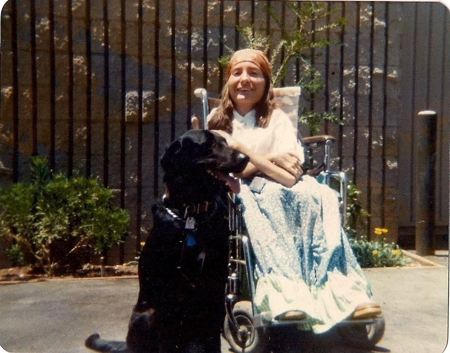 Old photograph of the first service dog team, a woman in a wheelchair with her arm around a black lab