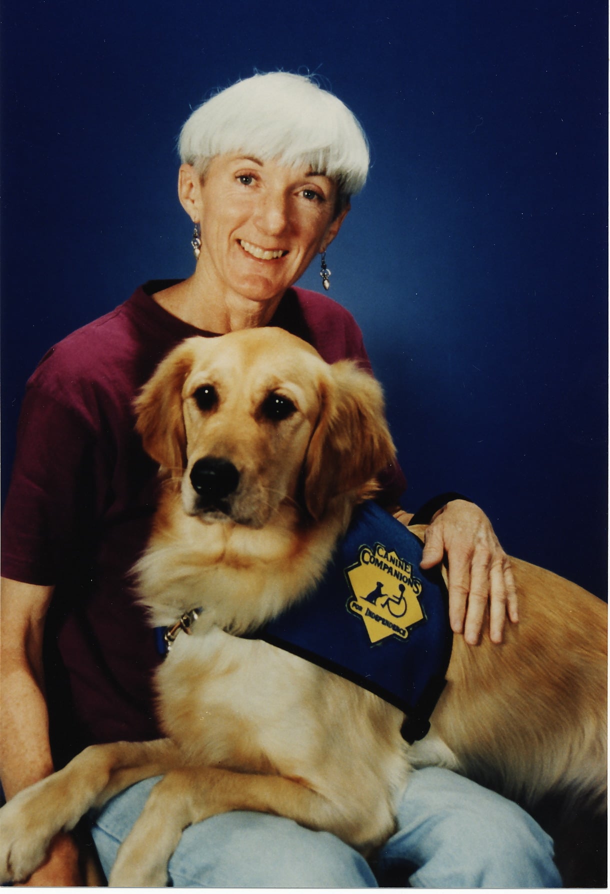photography of a woman with her arm around a golden retriever wearing a canine companions blue service vest