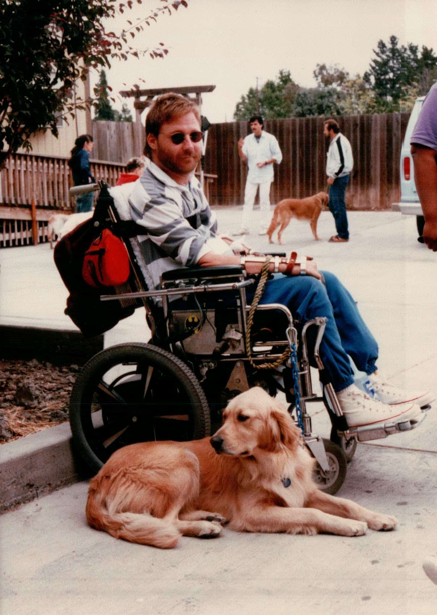 image of a man in a wheelchair with a golden retriever laying next to him