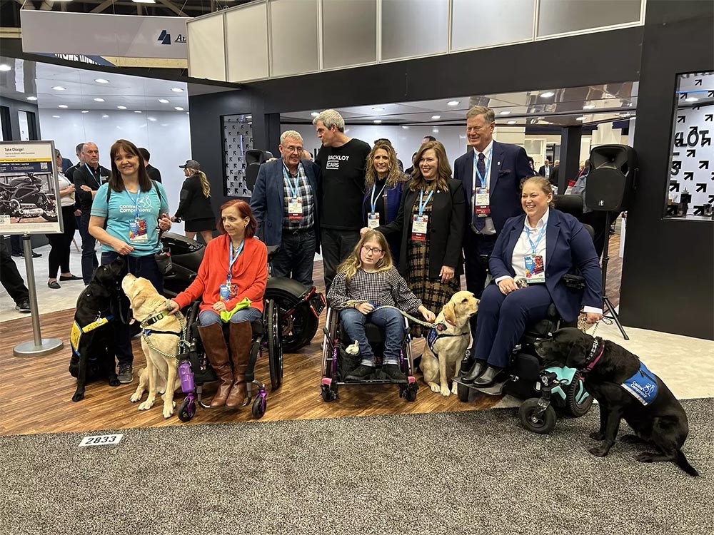 A group of people including graduates in wheelchairs and their service dogs pose at the NADA show