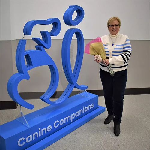 Image of a woman holding flowers next to a canine companions logo sign