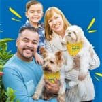 Man and woman with a young boy holding two small white fluffy dogs who are wearing yellow bandanas