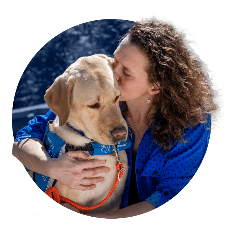 a woman kissing a yellow lab in a blue service dog vest
