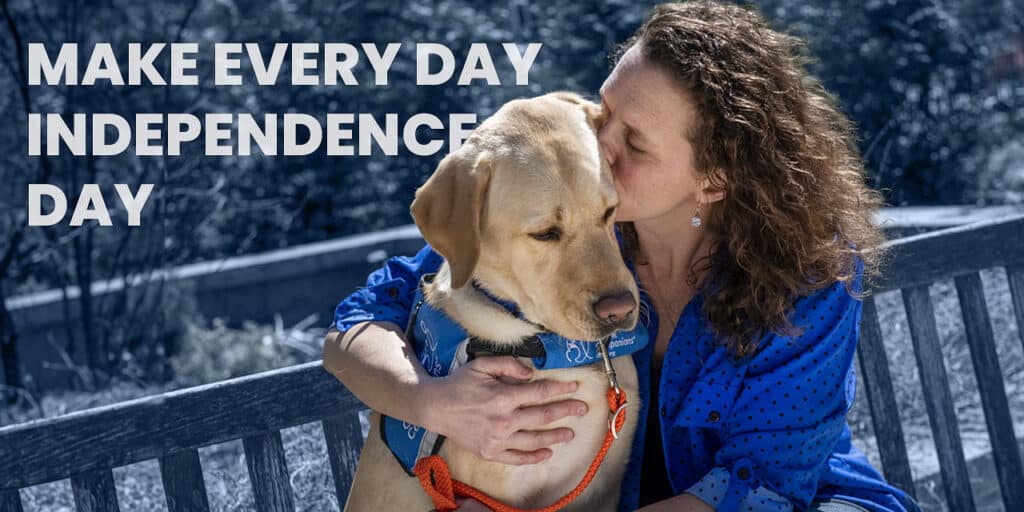 a woman sitting on a bench with her arm around and kissing on a Labrador, who is wearing a blue vest; the background text reads, Make Every Day Independence Day