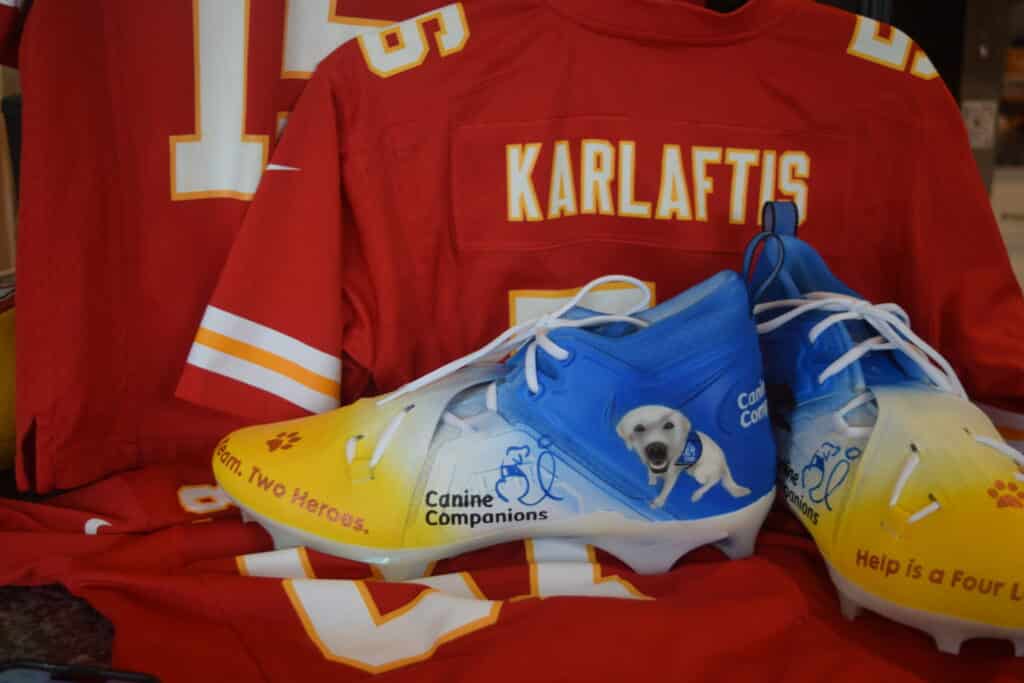 Canine Companions branded cleats sit in front of a George Karlaftis jersey