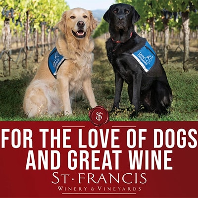 Two service dogs with blue Canine Companions vests sit in St. Francis Winery vineyard. Includes the campaign slogan “For the Love of Dogs and Great Wine.”