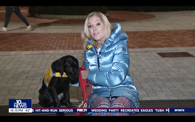 Woman reporter seating with a Canine Companions puppy