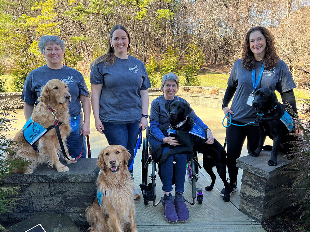 A group of smiling Canine Companions evaluators with therapy dogs