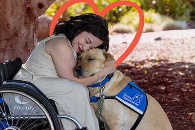 A woman hugging her service dog with red hearts in the background