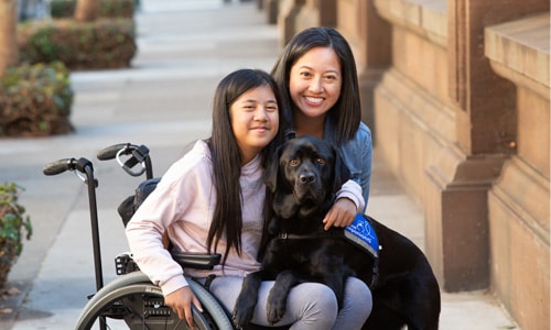 young girl in a wheelchair with her mom and her black canine companions service dog