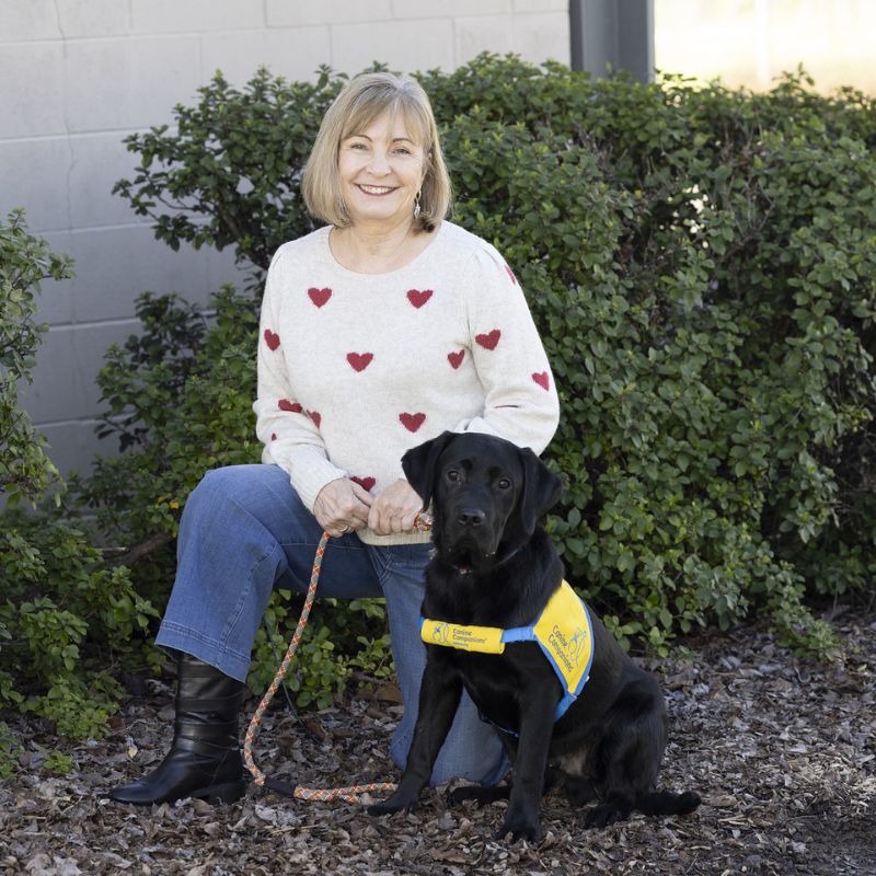 A smiling woman posing with a dog in a service vest