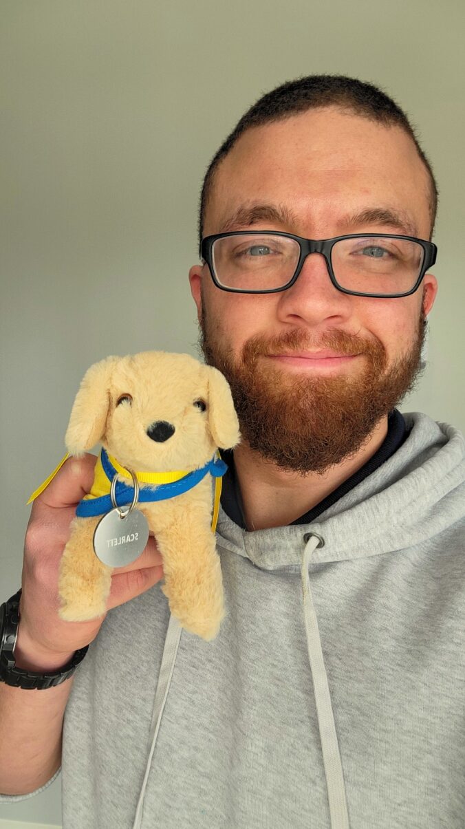 a smiling man holding a plush puppy with a name tag that says scarlett