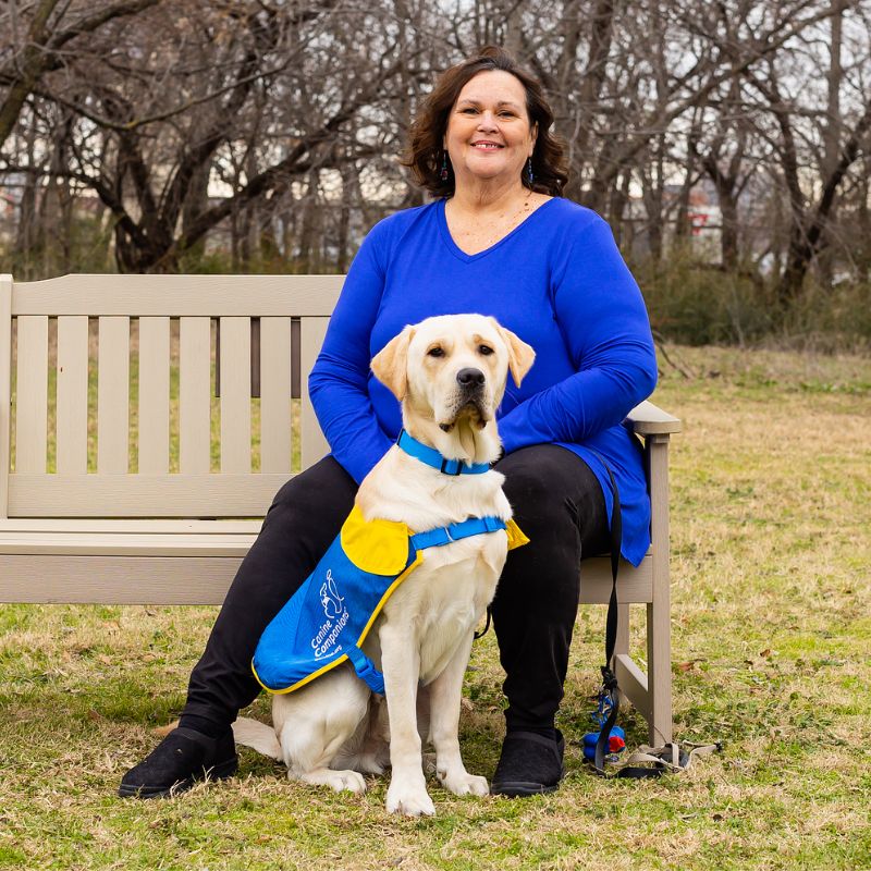 A smiling woman posing with a dog in a service vest