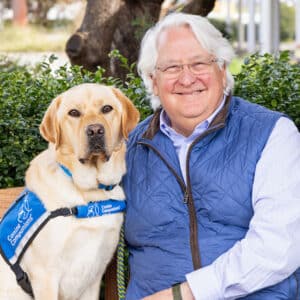 a smiling man sitting next to a yellow lab service dog