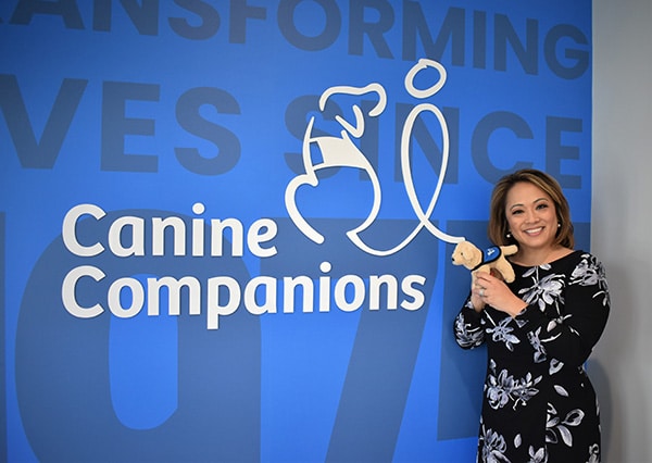 News Anchor Angela An in front of a wall with canine Companions logo