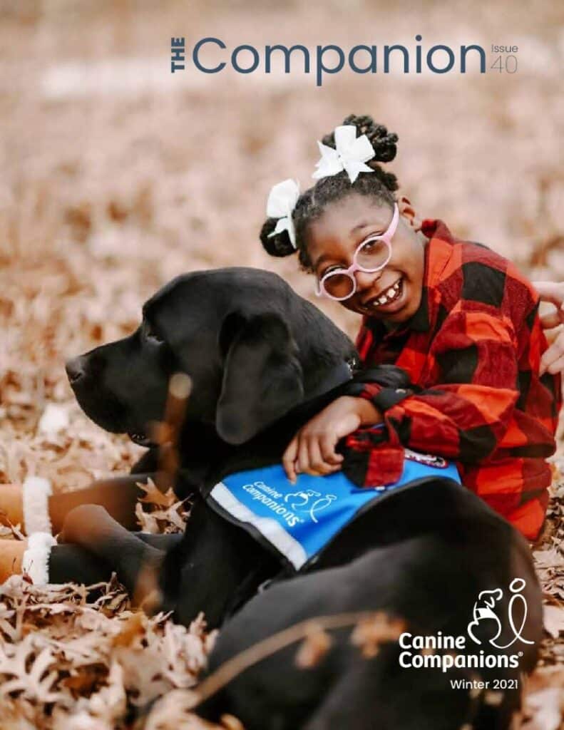 Cover of the 2021 winter Companion magazine featuring a smiling girl and her black lab service dog sitting in fall leaves