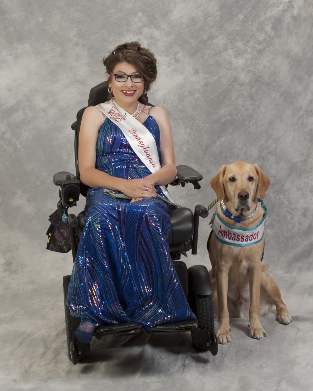 young woman in an evening dress seating in a wheelchair with her service dog seating next to her