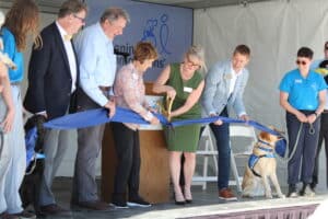 CEO Paige Mazzoni cuts ribbon with help of service dogs, Jean Schulz and others.