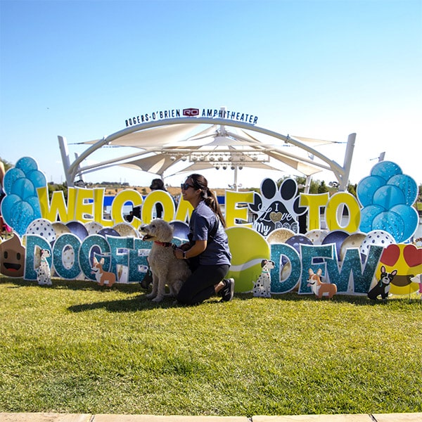 a woman with her poodle in front of a dogfest sign