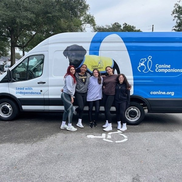 five smiling volunteers in front of a canine companions truck