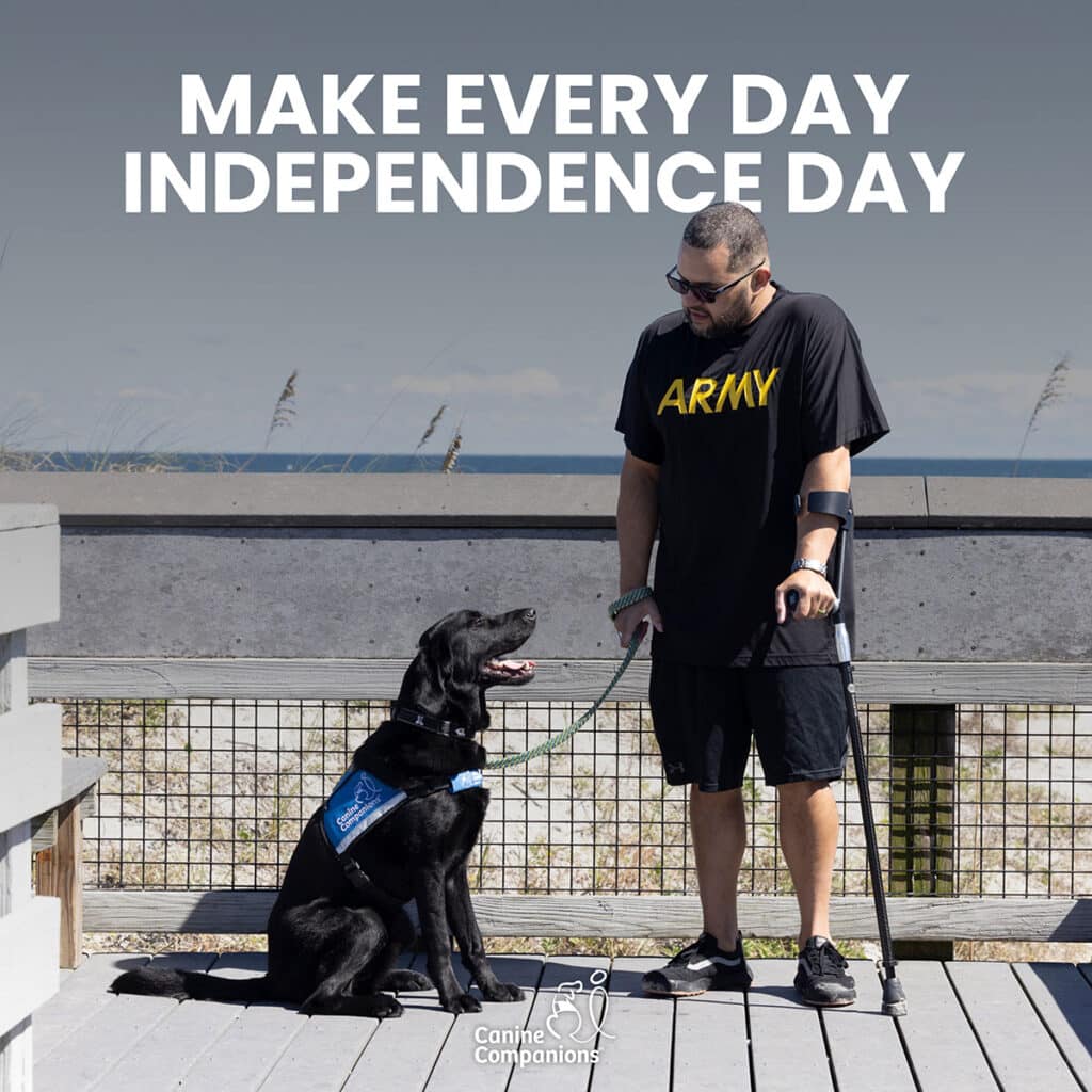 A man wearing an 'ARMY' T-shirt stands with his black service dog on a boardwalk by the beach. The text above them reads 'MAKE EVERY DAY INDEPENDENCE DAY' with the Canine Companions logo at the bottom.
