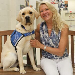 Woman sitting on a bench with a Labrador wearing a service dog vest.