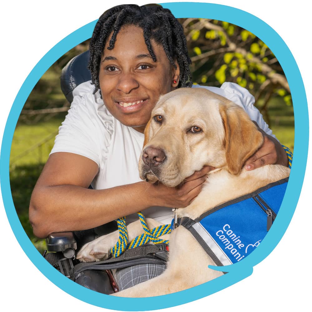 Person smiling and embracing a service dog wearing a blue "Canine Companions" vest.